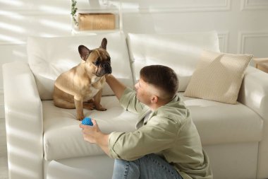 Evdeki kanepenin yanında sevimli köpeği ve oyuncağıyla genç bir adam.