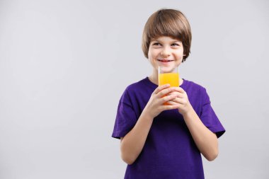 Açık gri arka planda bir bardak taze portakal suyu olan çocuk. Metin için boşluk