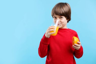 Açık mavi arka planda bir bardak taze portakal suyu ve meyveli çocuk. Metin için boşluk