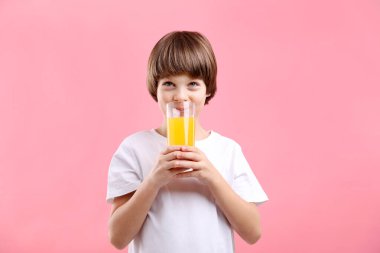 Pembe arka planda bir bardak taze portakal suyu olan çocuk.