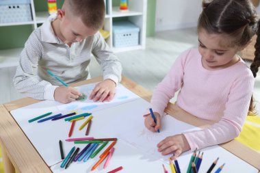 Çocuklar kalem ve pastel boyayla resim çiziyor.