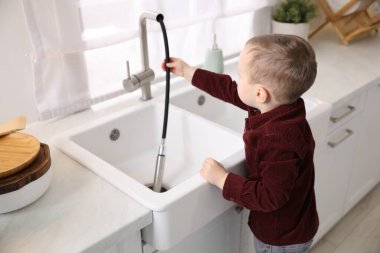 Evde çocuk güvenliği. Küçük çocuk mutfakta musluk hortumunu çekiyor.
