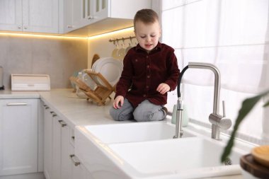 Evde çocuk güvenliği. Küçük çocuk mutfaktaki musluk hortumunu çekiyor.