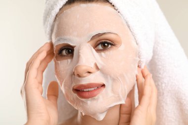 Saçları havluya sarılı ve açık gri arka planda maske takan kadın, yakın plan.