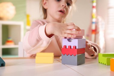 Oyun odasındaki beyaz masada oyuncaklarla oynayan mutlu küçük kız, seçici odaklanma