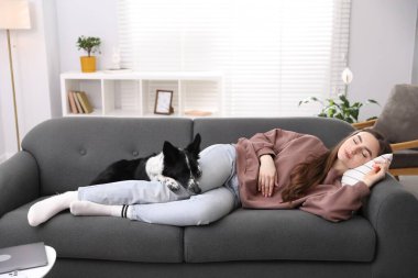 Evdeki kanepede uyuyan sevimli köpeğiyle genç bir kadın.