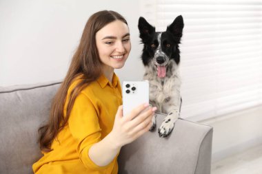 Sevimli köpeğiyle gülümseyen kadın evdeki kanepede selfie çekiyor.