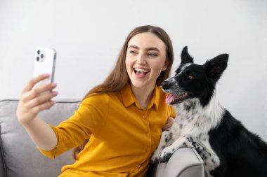 Sevimli köpeğiyle gülümseyen kadın evdeki kanepede selfie çekiyor.
