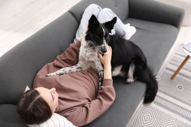 Evdeki kanepede sevimli köpeğiyle yatan bir kadın.