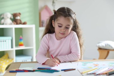 Masada pastel boyayla resim çizen sevimli küçük kız.