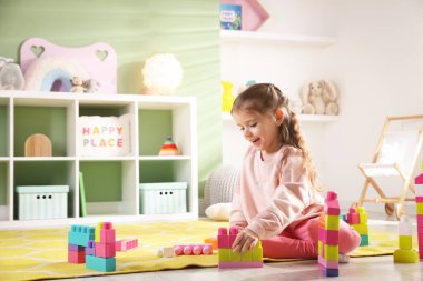 Küçük kız oyun odasında yerde oyuncaklarla oynuyor.