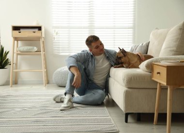 Evdeki kanepenin yanında tatlı köpeğiyle rahatlayan genç bir adam.