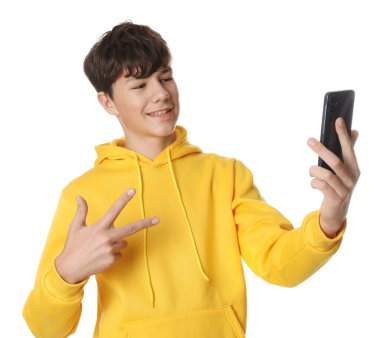 Genç çocuk beyaz arka planda selfie çekerken barış işareti gösteriyor.