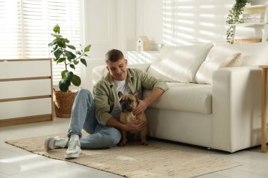 Evdeki kanepenin yanında tatlı köpeğiyle rahatlayan genç bir adam.