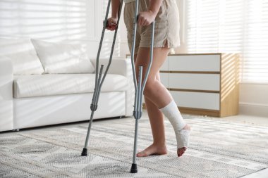 Woman with hurt leg using crutches at home, closeup