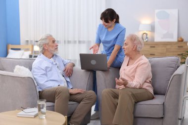 Bakım işçisi üst düzey erkek ve kadınlara huzurevinde dizüstü bilgisayar kullanmayı öğretiyor.