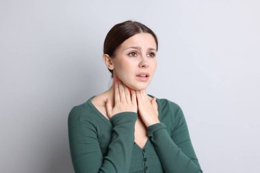 Gri arka planda boğaz ağrısı çeken bir kadın. Boynunda kırmızı bölge.