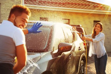 Mutlu çift araba yıkıyor ve güneşli bir günde arka bahçede eğleniyor.