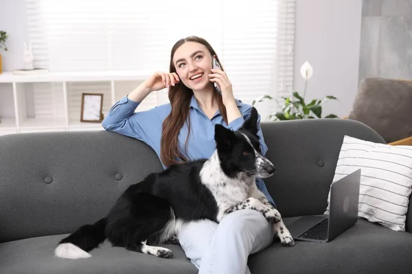 Akıllı telefonuyla gülümseyen bir kadın ve evdeki kanepede oturan sevimli köpeği.