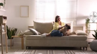 Evdeki kanepede sevimli köpeğini okşayan bir kadın.