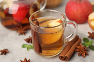 Cam fincanda aromatik meyve çayı, çaydanlık, elma, nane ve baharatlar gri masada, yakın plan.