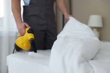 Haşere kontrol işçisi yatağı temizliyor, kapalı alanda buhar temizleyicisiyle, yakın plan