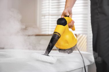 Haşere kontrol işçisi yatağı temizliyor, kapalı alanda buhar temizleyicisiyle, yakın plan