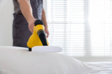 Haşere kontrol işçisi yatağı temizliyor, kapalı alanda buharlı temizleyiciyle, yakın plan. Metin için boşluk
