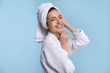 Saçları açık mavi arka planda havluya sarılı güzel bir kadın.