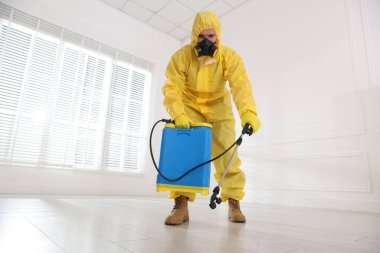 Koruyucu giysiler içinde böcek ilacı sıkan haşere kontrol görevlisi, düşük açılı.