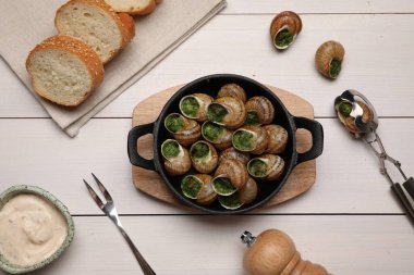 Beyaz ahşap masada servis edilen nefis pişmiş salyangozlar.