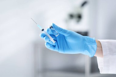 Hafif arka planda aşı ve şırınga şişesi olan hemşire, yakın plan.