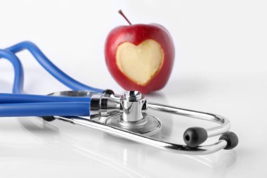 Yüreği oyulmuş olgun elma ve steteskop beyaz masada, yakın plan.