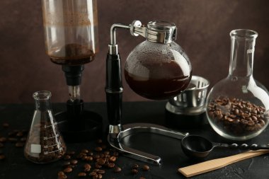 Kahve makineli sifon (vakum) kahve makinesi ve kahve bardağı ile siyah masanın üzerindeki fasulyeler kahverengi arka planda, yakın plan