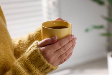 Sarı fincanı elinde tutan kadın, kapalı alanda çay içen, yakın plan.