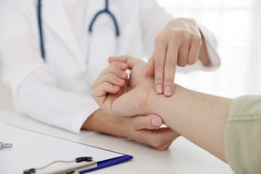 Doktor masadaki parmaklarıyla adamın nabzını kontrol ediyor.