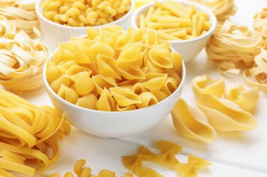 Beyaz ahşap masa üzerinde farklı türde ham makarna, yakın plan.