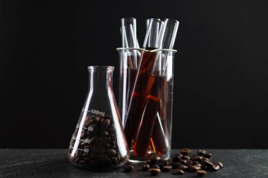 Siyah masada kahve ve fasulye bulunan laboratuvar bardakları.