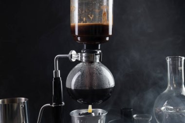 Vakumlu kahve makinesinde aromatik kahve demlemek siyah arka planda, dumanlı, yakın plan.