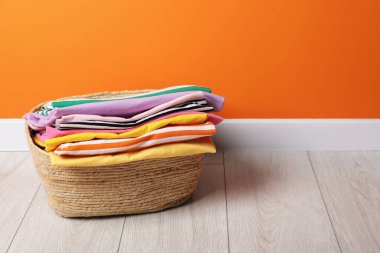 Çamaşır sepetinde yerde giysiler var. Kapalı alanda turuncu duvarın yanında. Mesaj için yer var.