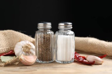 Ahşap masada baharatlı tuzluklar ve biberlikler siyah arka planda, yakın plan