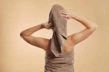 Bej arka planda, havluya sarılı saçları olan kadın.