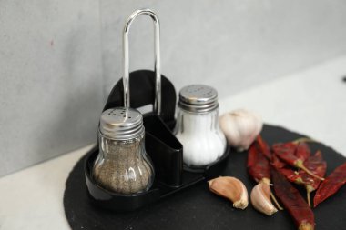 Gri duvarın yanındaki beyaz masada baharatlı tuzluk ve biberlikler, yakın plan.