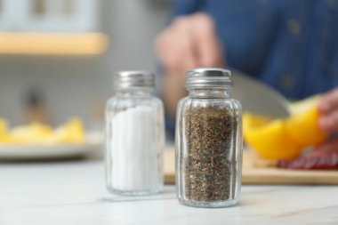Beyaz mermer masada tuzluk ve biberlikle yemek pişiren bir kadın. Kapalı mekanda baharatlar, seçici bir odak noktası.