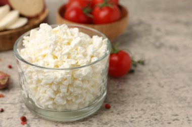 Cam kasede taze süzme peynir, gri masada domates ve baharatlar, yakın plan.