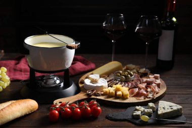 Nefis erimiş peynir fondü kabında, abur cubur ve şarap ahşap masada, siyah arka planda, yakın planda.