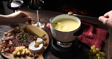 Bir çift ekmek ve üzümü fondü kabına daldırmak ahşap masada lezzetli erimiş peynirle siyah arka planda atıştırmalıklar, yakın plan