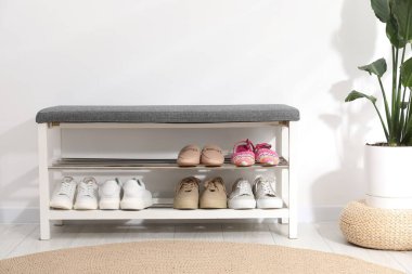 Ayakkabı bankı, farklı ayakkabılar ve beyaz duvarın yanında ev bitkisi.