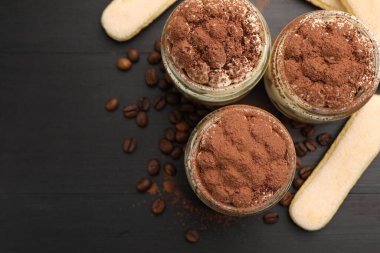 Kavanozlarda nefis tiramisu, savoiardi bisküvileri ve koyu ahşap masa üzerinde kahve çekirdekleri. Metin için boşluk