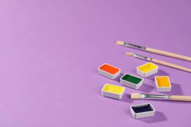 Mor arka planda suluboya tavalar ve fırçalar, yakın plan. Metin için boşluk